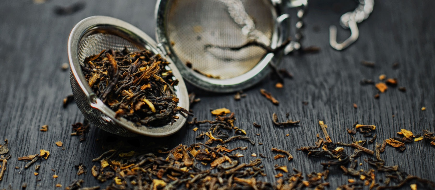 dry tea leaves and stems in a tea infuser or expired tea with rusty black wooden background.