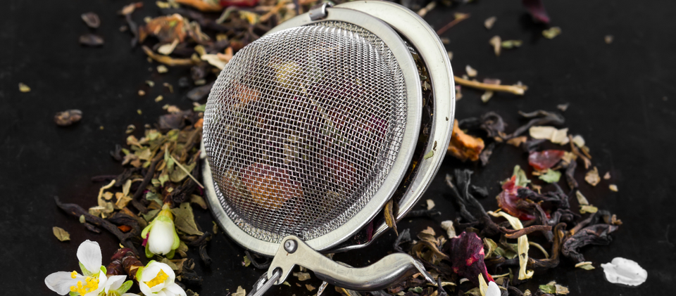 Herbal tea and tea leaves with flowers in a tea strainer, and black background.