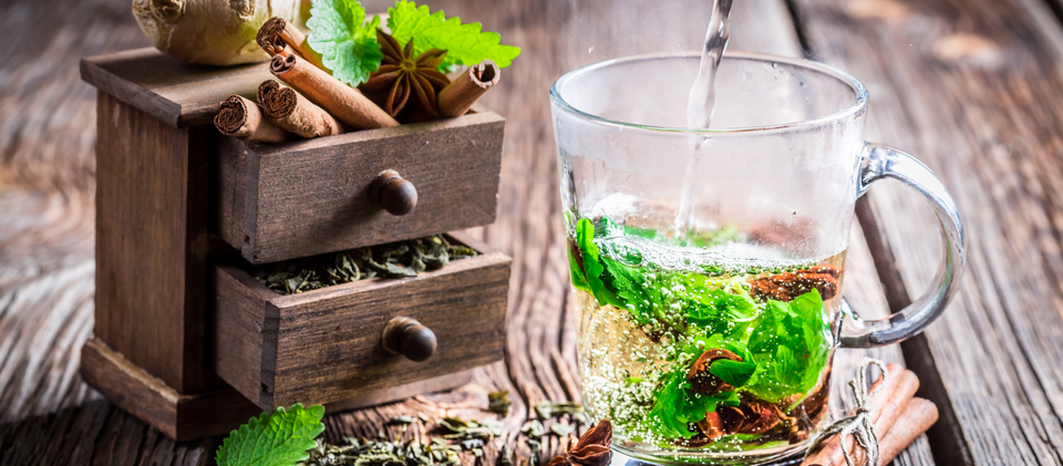 Brewing green tea with cinnamon, green tea leaves, ginger, dry leaves, and a wooden small drawer filled with ingredients with wooden background.