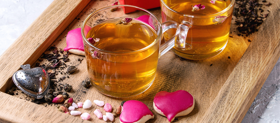 Two cups of valentine tea in a wooden tray with a rusty black background, pink hearts, pink flowers all over the place.