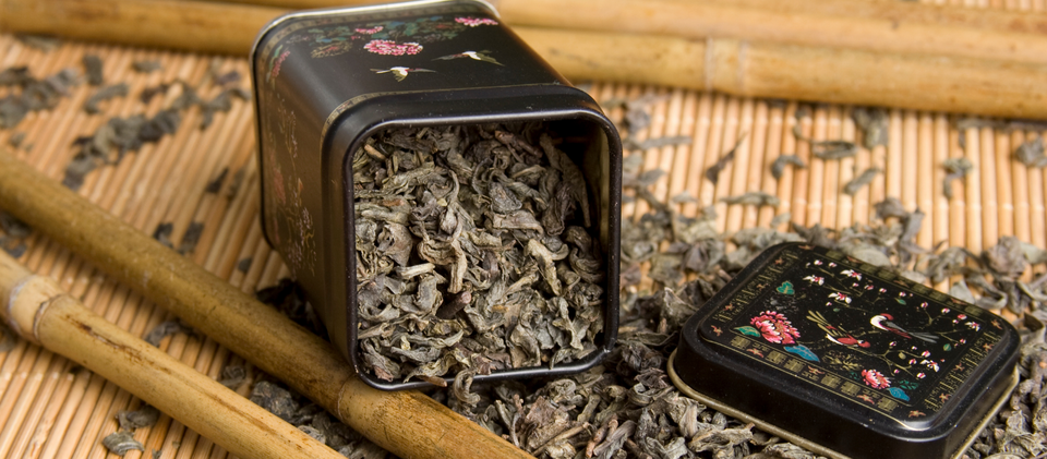 Black Tea storage box or tea container with dry loose tea leaves, light brown background and wooden stick.