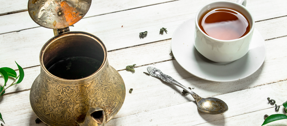 ancient kettle, spoon, white wooden background with a white teacup on a white plate and green leaves.